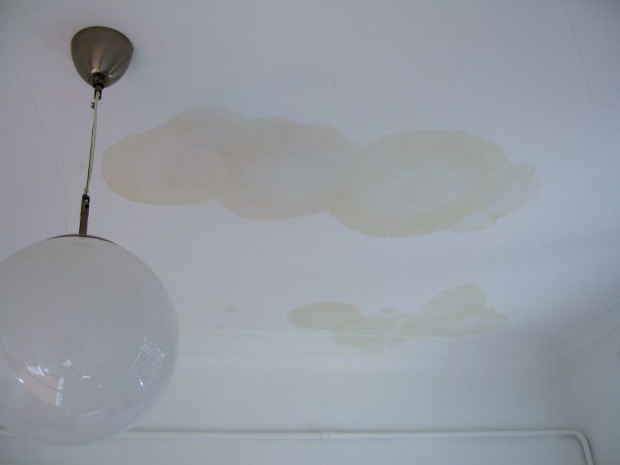 Ceiling water stains around a hanging light fixture from a roof leak inside a room