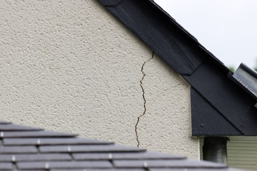 Cracked stucco exterior wall beneath roof eaves on a house