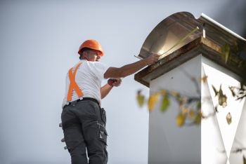 Construction worker in hard hat and safety vest cleaning a chimney on a roof